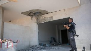 شرطي إسرائيلي يتفقد الأضرار التي لحقت لموقع بناء في  بلدة سديروت الواقعة جنوب إسرائيل بالقرب من الحدود مع غزة في أعقاب سقوط صاروخ في الموقع، 9 أغسطس، 2018.  (Yonatan Sindel/Flash90)