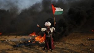 امرأة فلسطينية ترفع العلم أمام إطارات محترقة خلال اشتباكات على طول السياج الحدودي، شرق مدينة غزة في 28 سبتمبر 2018. ( AFP PHOTO / Said KHATIB)
