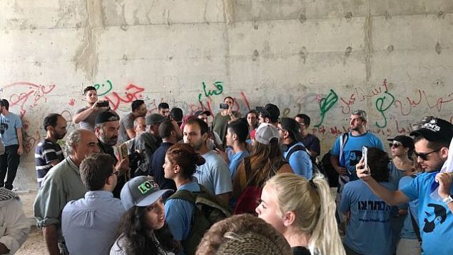 ناشطون يمينيون إسرائيليون يرتدون قمصانا زرقاء يتبادلون الهتافات مع نشطاء فلسطينيين وسكان محليين في ممر تحت الطريق السريع 1 بالقرب من قرية الخان الأحمر البدوية في الضفة الغربية، 7 سبتمبر / أيلول 2018. (لقطة شاشة: تويتر)