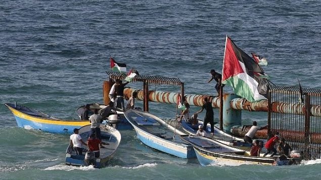 متظاهرون فلسطينيون على متن قوارب يرفعون الاعلام الفلسطينية على مبنى حديدي عند الحدود البحرية مع اسرائيل، في شمال قطاع غزة، 8 اكتوبر 2018 (AFP PHOTO / Said KHATIB) متظاهرون فلسطينيون على متن قوارب يرفعون الاعلام الفلسطينية على مبنى حديدي عند الحدود البحرية مع اسرائيل، في شمال قطاع غزة، 8 اكتوبر 2018 (AFP PHOTO / Said KHATIB)