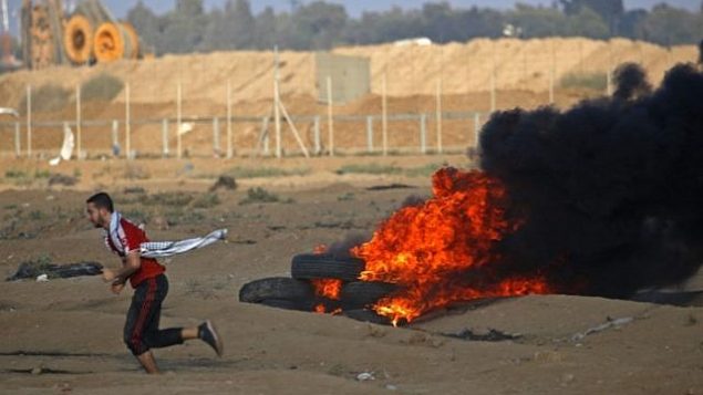 محتج فلسطيني يركض بجانب إطارات محترقة على الحدود بين إسرائيل وغزة، شرق مدينة غزة، في 12 أكتوبر 2018. (Said KHATIB / AFP)
