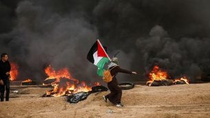 امرأة فلسطينية ترفع العلم الفلسطيني وسط دخان أسود من الإطارات التي أحرقها المتظاهرون، خلال اشتباكات قرب الحدود مع إسرائيل شرق مدينة غزة في 26 أكتوبر 2018. (MAHMUD HAMS / AFP)