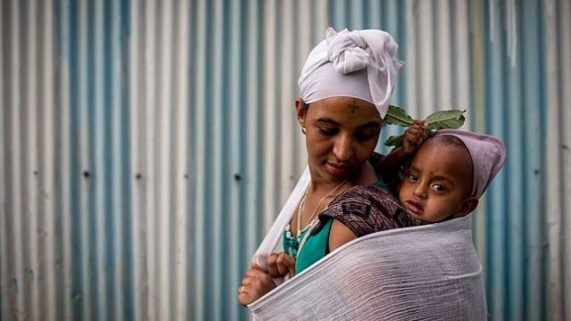 إمرأة في جماعة الفلاشا اليهودية الإثيوبية تحمل طفلها على ظهرها قبل حضور الصلاة في عيد الفصح، في الكنيس في غوندار، إثيوبيا. 22 أبريل 2016. (Miriam Alster/FLASH90)