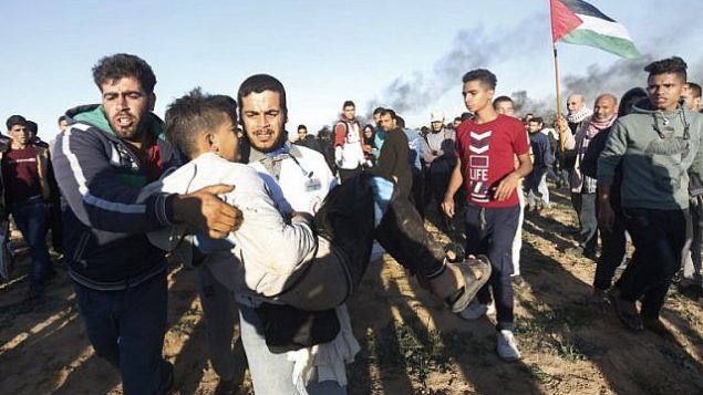 فلسطيني يحمل شاباً بعيداً عن التظاهرات على الحدود بين إسرائيل وخان يونس في جنوب قطاع غزة، في 14 ديسمبر / كانون الأول 2018. (Said Khatib/AFP) فلسطيني يحمل شاباً بعيداً عن التظاهرات على الحدود بين إسرائيل وخان يونس في جنوب قطاع غزة، في 14 ديسمبر / كانون الأول 2018. (Said Khatib/AFP)