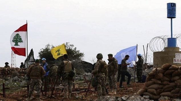 صورة التقطت من قرية ميس الجبل اللبنانية، تظهر جنود اسرائيليون يراقبون بينما جنود قوات حفظ السلام الأممية يتحدثون مع جنود لبنانيين امام علم حزب الله، 16 ديسمبر 2018 (Mahmoud ZAYYAT / AFP)