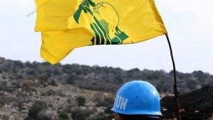 صورة تم التقاطها من قرية ميس الجبل في 16 ديسمبر، 2018، تظهر فيها جنديا تابعا لقوات الأمم المتحدة المؤقتة في لبنان (يونيفيل) يقوم بمراقبة الحدود بين لبنان وإسرائيل. على يمينه علم  لمنظمة ’حزب الله’ اللبنانية الشيعية. (Mahmoud Zayyat/AFP)
