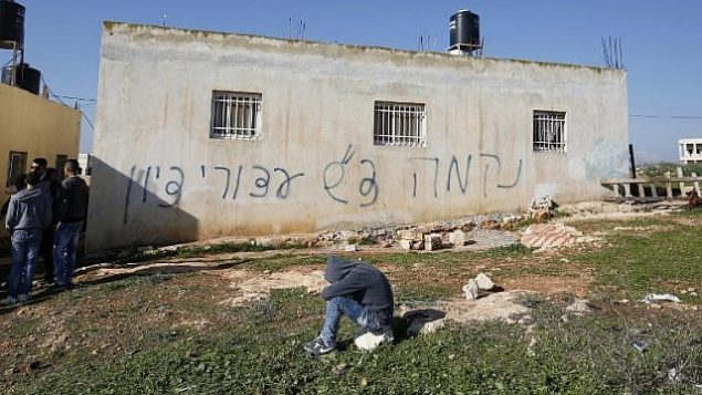 فلسطينيون يحتشدون بالقرب من منزل خط عليه عبارات ’انتقام’ و’تحية من أسرى صهيون’، في قرية بيت إللو في الضفة الغربية، 22 ديسمبر، 2015. (AFP PHOTO/ABBAS MOMANI)