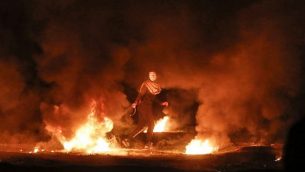 فلسطيني ملثم يقوم بسحب إطار مشتعل خلال مظاهرة ليلية بالقرب من السياج الحدودي مع إسرائيل، شرق مدينة غزة، 11 فبراير، 2019. (Mahmud Hams/AFP)