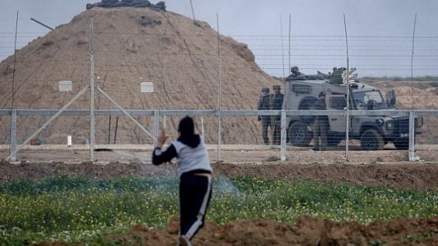 فلسطيني يستخدم مقلاعا لإلقاء أشياء باتجاه القوات الإسرائيلية بالقرب من سيارة مدرعة على الجانب الآخر من السياج الشائك على الحدود مع إسرائيل شرق مدينة غزة في 1 مارس 2019. (Said KHATIB / AFP)
