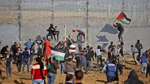 فلسطينيون يرفعون أعلاما فلسطينية خلال محاولتهم تسلق السياج الأمني على الحدود بين إسرائيل وقطاع غزة، شرق مدينة غزة، 22 مارس، 2019.   (Said Khatib/AFP)