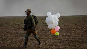 توضيحية: جندي إسرائيلي يقف بجانب بالونات أطلقها متظاهرون فلسطينيون من قطاع غزة وهبطت داخل إسرائيل في 19 أكتوبر، 2018. (Yossi Zamir/Flash90)