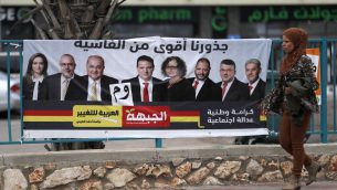 سيدة عربية اسرائيلية تمر امام لافتة انتخابية تظهر مرشحين عرب اسرائيليين في كفر مندا (AHMAD GHARABLI / AFP)