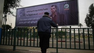 شرطي فلسطيني تابع لحركة "حماس" ينظر إلى لافتة تحمل صورة الجندي الإسرائيلي القتيل أورون شاؤول في مدينة غزة، 29 ديسمبر، 2017، كُتب عليها بالعربية: "طالما أبطالنا لا يرون الحرية والنور، هذا الأسير لن يرى الحرية أبدا".  (AFP PHOTO / MOHAMMED ABED)