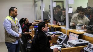 موظفو بريد يساعدون فلسطينيين وصلوا إلى مكتب البريد الرئيسي في مدينة غزة في 26 يناير، 2019 للحصول على أموال مساعدات من الحكومة القطرية للعائلات المحتاجة. (Mahmud Hams/AFP)