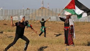 متظاهر فلسطيني يرشق القوات الإسرائيلية بحجارة وامراة ترتدي زيا فلسطينيا تقليديا تلوح بالعلم الفلسطيني، خلال تظاهرة بالقرب من الحدود مع إسرائيل، شرق مدينة غزة، 10 مايو، 2019. (Said KHATIB / AFP)