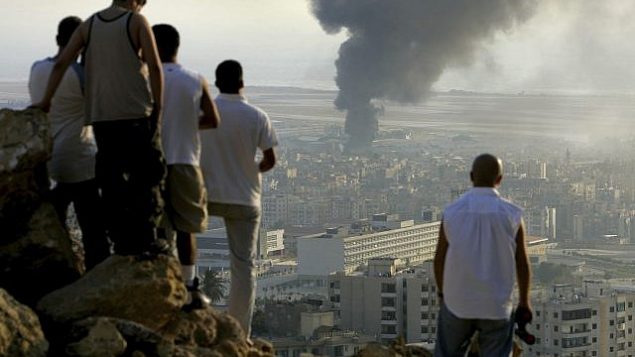 في هذه الصورة من تاريخ 14 يوليو، 2006، يظهر شبان لبنانينون يقفون على قمة تل يطل على مدينة بيروت في لبنان عند غروب الشمس لمشاهدة الدخان المتصاعد من مضخة وقود في مطار بيروت الدولي، الذي تعرض لغارة جوية إسرائيلية. (AP Photo/Ben Curtis)