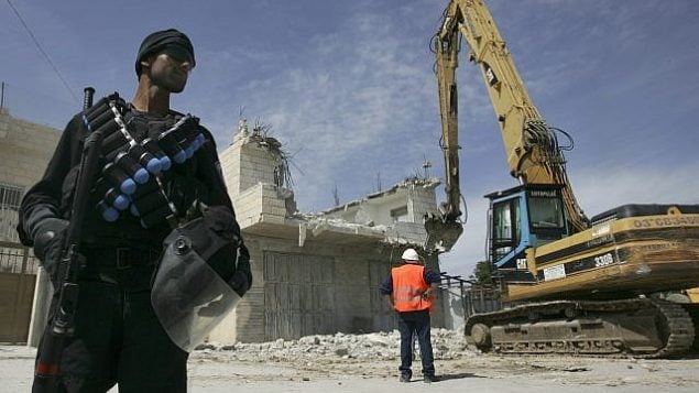 توضيحية: شرطي إسرائيل يقف بالقرب من جرافة خلال هدم منزل فلسطيني في حي صور باهر بالقدس الشرقية، 7 أبريل، 2009.  (Kobi Gideon / FLASH90)