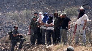 مستوطنون ملثمون إسرائيليون من يتسهار وجنود يراقبون حقولا فلسطينية تم إشعال النار في قرية عصيرة القبلية، 2 يونيو، 2010.  (Wagdi Ashtiyeh/Flash90)