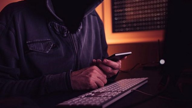 صورة توضيحية لهاكر يستخدم هاتفا ذكيا.   (stevanovicigor; iStock by Getty Images)