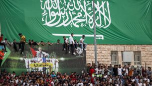 مشجعو كرة القدم يقفون تحت راية عملاقة تصور العلم السعودي خلال مباراة التصفيات الآسيوية المؤهلة لكأس العالم 2022 بين فلسطين والسعودية في بلدة الرام بالضفة الغربية، 15 اكتوبر 2019 (Ahmad GHARABLI / AFP)