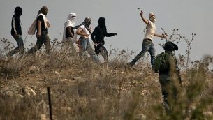 صورة توضيحية: جنود إسرائيليون يقفون امام مستوطنين إسرائيليين ملثمين يقومون بإلقاء الحجارة على متظاهرين فلسطينيين، خلال مظاهرة ضد البناء في بؤرة استياطنية إسرائيلية بالقرب من قرية ترمسعيّا الفلسطينية ومستوطنة شيلو، شمال رام الله في الضفة الغربية ، 17 أكتوبر 2019 (JAAFAR ASHTIYEH / AFP)