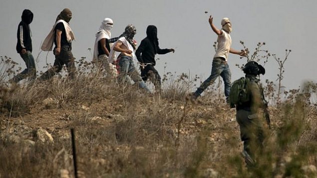 صورة توضيحية: جنود إسرائيليون يقفون امام مستوطنين إسرائيليين ملثمين يقومون بإلقاء الحجارة على متظاهرين فلسطينيين، خلال مظاهرة ضد البناء في بؤرة استياطنية إسرائيلية بالقرب من قرية ترمسعيّا الفلسطينية ومستوطنة شيلو، شمال رام الله في الضفة الغربية ، 17 أكتوبر 2019 (JAAFAR ASHTIYEH / AFP)
