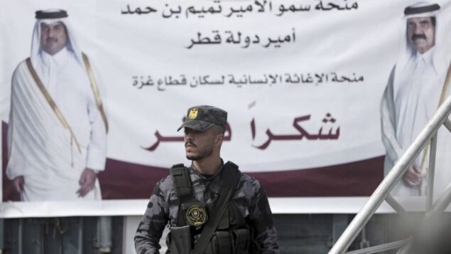 عضو من حماس يقف على أهبة الاستعداد أمام ملصق لأمير قطر، الشيخ تميم بن حمد آل ثاني، يسار، والأمير السابق لقطر، الشيخ حمد بن خليفة آل ثاني، خلال مؤتمر صحفي مع ماتياس شماليه، مدير الأونروا في غزة، والمبعوث القطري، محمد العمادي، في مستشفى الشفاء في مدينة غزة، 19 فبراير 2018 (AP Photo / Khalil Hamra)