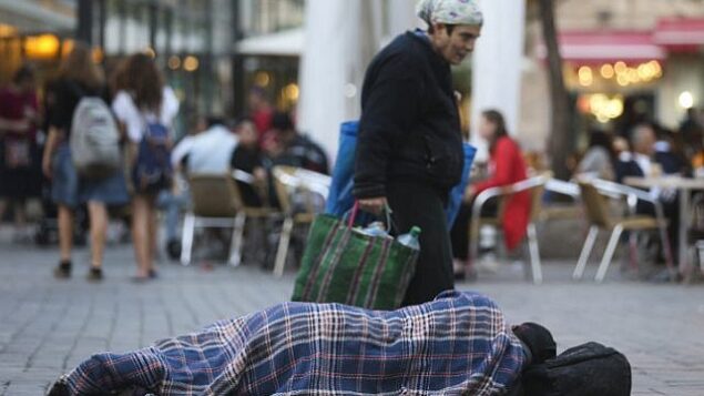 أشخاص يمرون من أمام رجل مشرد بالقرب من مقاهي في وسط مدينة القدس، 10 نوفمبر، 2013.  (Nati Shohat/FLASH90)