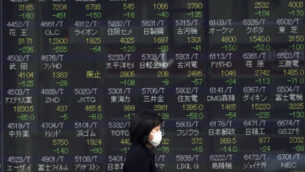 صورة توصيحية: امرأة تسير امام لوحة أسهم إلكترونية تعرض مؤشر Nikkei 225 الياباني في إحدى شركات الأوراق المالية في طوكيو، 25 فبراير 2020 (AP / Eugene Hoshiko)