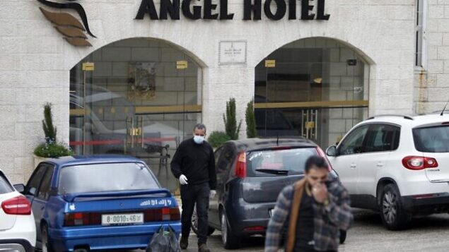 رجال فلسطينيون، أحدهم يضع قناعا واقيا، يغادرون فندق Angel في بيت مدينة لحم بالضفة الغربية قي بيت لحم، 6 مارس، 2020. (Musa Al Shaer/AFP)