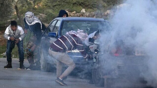 شبان فلسطينيون يحتمون وسط الدخان المسيل للدموع خلال مواجهات مع القوات الإسرائيلية في قرية بجنوب غزة في الضفة الغربية، 11 مارس، 2020. ( JAAFAR ASHTIYEH / AFP)