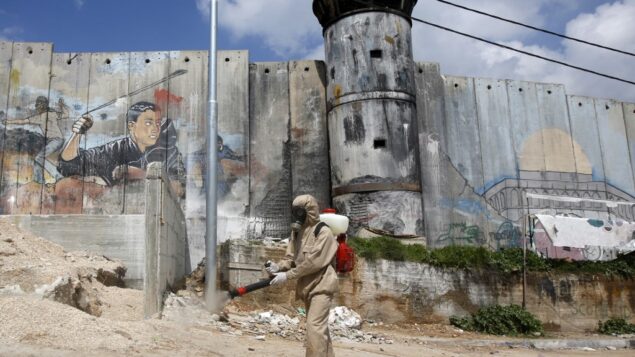 عامل نظافة فلسطيني يرش مطهرًا حول مخيم عايدة للاجئين بالقرب من بيت لحم، 16 مارس 2020 (Musa Al SHAER / AFP) عامل نظافة فلسطيني يرش مطهرًا حول مخيم عايدة للاجئين بالقرب من بيت لحم، 16 مارس 2020 (Musa Al SHAER / AFP)