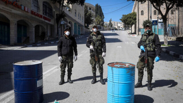 عناصر في قوى الأمن الفلسطينية تضع أقنعة وتغلق مدخل مدينة بيت لحم بالضفة الغربية،  8 مارس، 2020.  (Wisam Hashlamoun/Flash90)