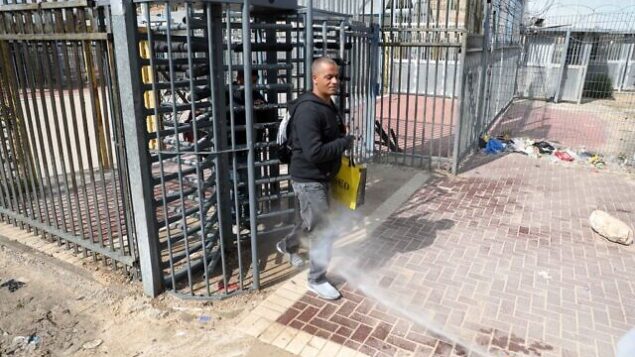 عمال صحة فلسطينيون يقومون بإجراء تعقيم لعمال فلسطينيين عائدين من إسرائيل عند حاجز في ترقوميا، ٫ 25 مارس، 2020. (Wisam Hashlamoun/Flash90)