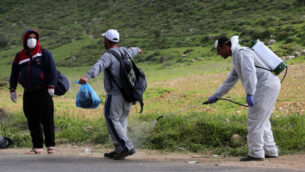 عمال صحة فلسطينيون يقومون بإجراء تعقيم لعمال فلسطينيين عند عودتهم من إسرائيل عند حاجز في ترقميا، 25 مارس، 2020.  (Wisam Hashlamoun/Flash90)