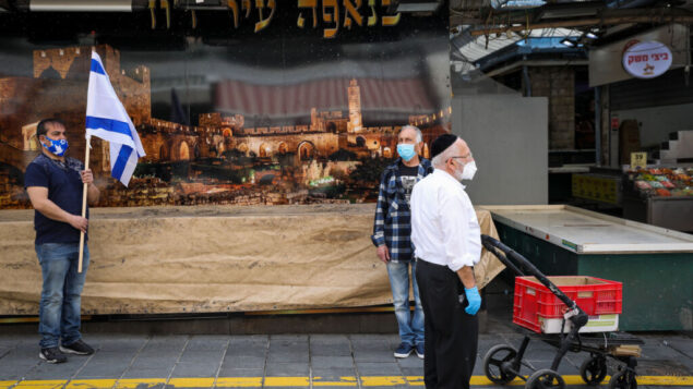 اشخاص يقفون في سوق محانيه يهودا في القدس، اثناء انطلاق صفارات الإنذار لمدة دقيقتين في جميع أنحاء إسرائيل بمناسبة يوم ذكرى المحرقة، 21 أبريل 2020 (Olivier Fitoussi / Flash90)