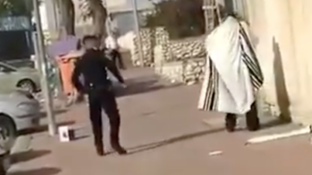 لقطة من مقطع فيديو يوثق قيام شرطي برش رجل حريدي من نتنيفوت برذاذ الفلفل خلال قيام الأخير بالصلاة خارج منزله في 7 أبريل، 2020. (Screen capture/TikTok)