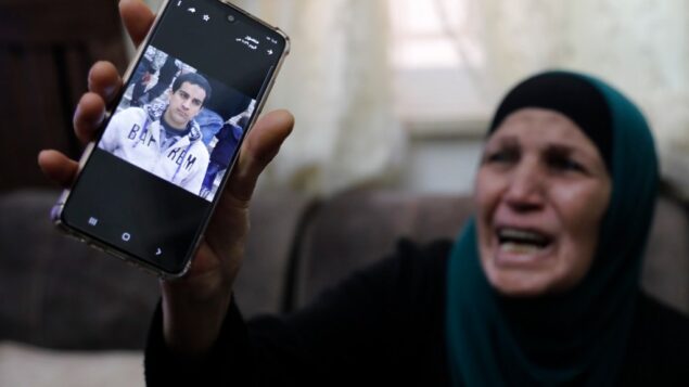 والدة رجل فلسطيني من ذوي الاحتياجات الخاصة، قالت الشرطة إنه قتل بالرصاص بعد اعتقادها خطأً أنه مسلح بمسدس، تبكي وهي تظهر صورتها على هاتفها الخليوي، في منزلها في القدس الشرقية، 30 مايو 2020. (Ahmad GHARABLI / AFP)