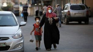 سيدة فلسطينية تحمل طبقًا من الطعام وهي تمشي جنبًا إلى جنب مع طفلها  وهما يرتديان كمامات، في مدينة غزة ، 28 أغسطس، 2020، خلال إغلاق في القطاع الفلسطيني بسبب تزايد حالات الإصابة بفيروس كورونا. (Mohammed Abed/AFP)