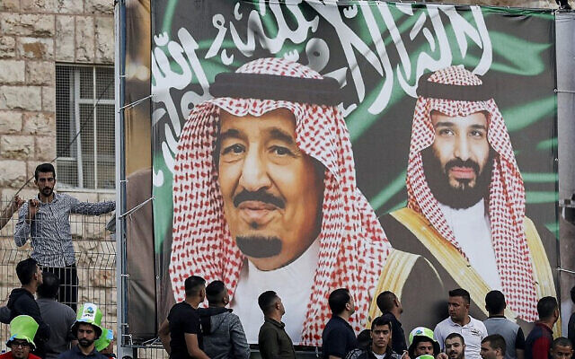 مشجعو كرة القدم يقفون تحت راية عملاقة تصور الملك السعودي سلمان بن عبد العزيز (وسط) ونجله ولي العهد الأمير محمد بن سلمان (يمين) خلال مباراة التصفيات الآسيوية المؤهلة لكأس العالم 2022 بين فلسطين والسعودية في بلدة الرام بالضفة الغربية، 15 اكتوبر 2019 (Ahmad GHARABLI / AFP)