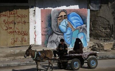 رجل فلسطيني وزوجته يركبان عربة يجرها حمار أمام فن الشارع يمران من أمام رسم على الحائط لطبيبين يرتديان الكمامة بسبب جائحة كوفيد -19 في مخيم النصيرات وسط قطاع غزة، 16 نوفمبر، 2020. (MOHAMMED ABED / AFP)