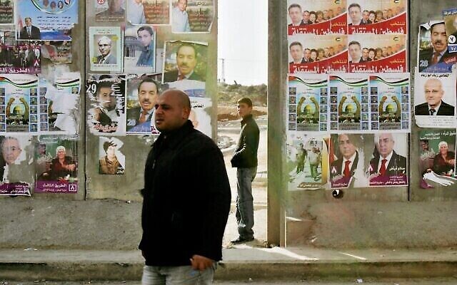 فلسطيني يمر من أمام قسم من الجدار الفاصل الإسرائيلي مغطى بملصقات حملة الانتخابات البرلمانية الفلسطينية في قرية الرام بالضفة الغربية، في ضواحي القدس، 23 يناير، 2006. (AP / Oded Balilty)