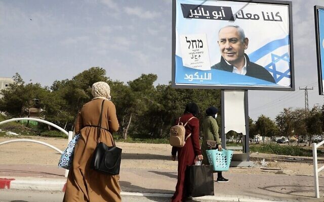 نساء بدويات يمرن أمام لوحات إعلانية لحزب الليكود الإسرائيلي اليميني تظهر صورة رئيس الوزراء بنيامين نتنياهو، في بلدة رهط البدوية بالقرب من مدينة بئر السبع جنوب إسرائيل، 10 مارس 2021 (HAZEM BADER / AFP)