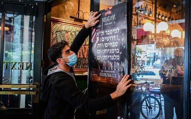 عامل يضع ملصقا إعلانيا للبحث عن عاملين في مطعم في تل أبيب، 3 مارس، 2021. (Avshalom Sassoni / Flash90)