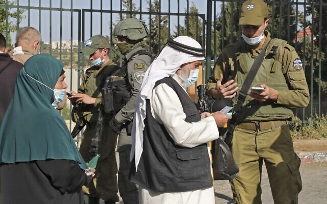 جنود إسرائيليون يتحققون من شهادات التطعيم ضد فيروس كورونا للفلسطينيين الذين يدخلون القدس لحضور صلاة الجمعة الأولى من شهر رمضان في المسجد الأقصى، عند حاجز بالقرب من بلدة بيت لحم بالضفة الغربية، 16 أبريل 2021 (Hazem BADER / AFP)