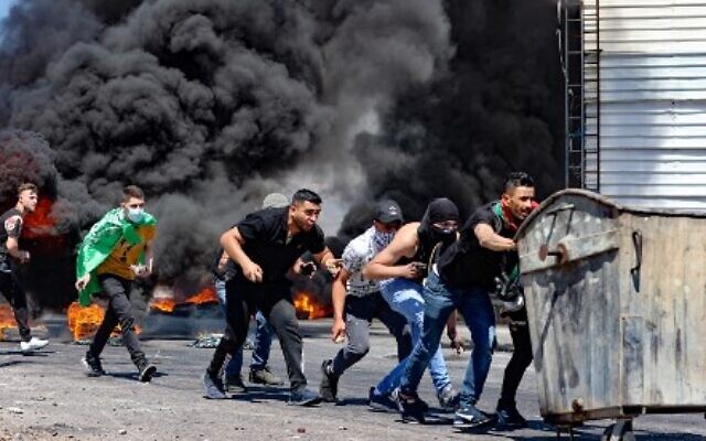 فلسطينيون يدفعون حاوية نفايات خلال مواجهات مع قوات الأمن الإسرائيلية بالقرب من حاجز حوارة جنوب مدينة نابلس بالضفة الغربية ،  14 مايو ، 2021 (Photo by JAAFAR ASHTIYEH / AFP)