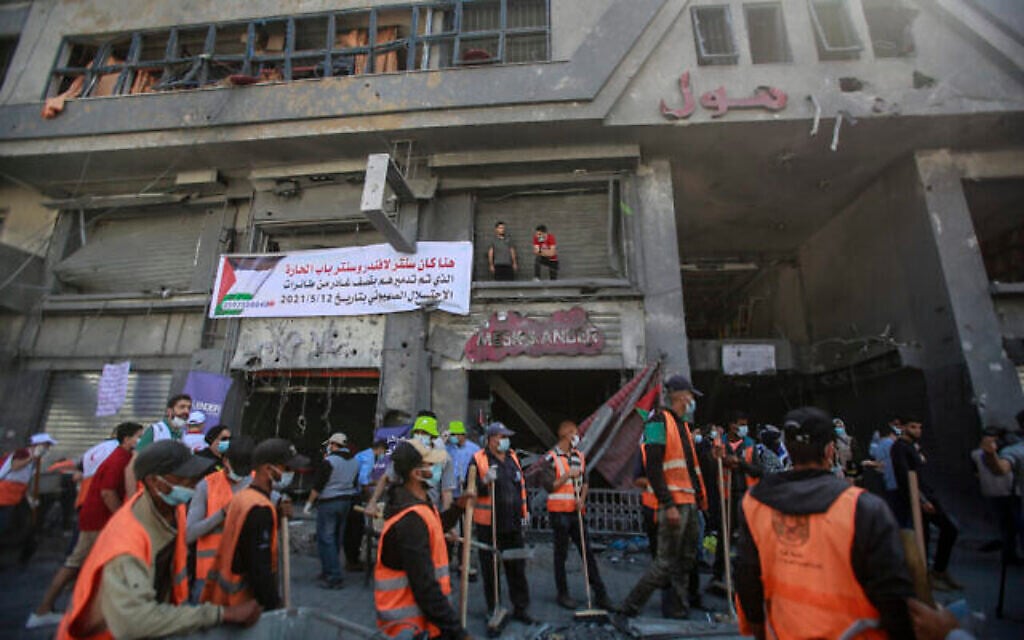 متطوعون فلسطينيون يزيلون الأنقاض في شارع بمدينة غزة، بعد أن أصابته غارات جوية إسرائيلية أثناء عملية ’حارس الأسوار’، 23 مايو، 2021. (Atia Mohammed / Flash90)