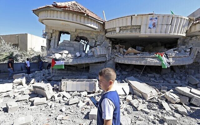 طفل فلسطيني يمر أمام مبنى يعود لمنتصر شلبي، المتهم بقتل طالب إسرائيلي في هجوم في مايو، بعد أن دمرته القوات الإسرائيلية في قرية ترمسعيا بالقرب من رام الله في الضفة الغربية، 8 يوليو، 2021.  (JAAFAR ASHTIYEH / AFP)