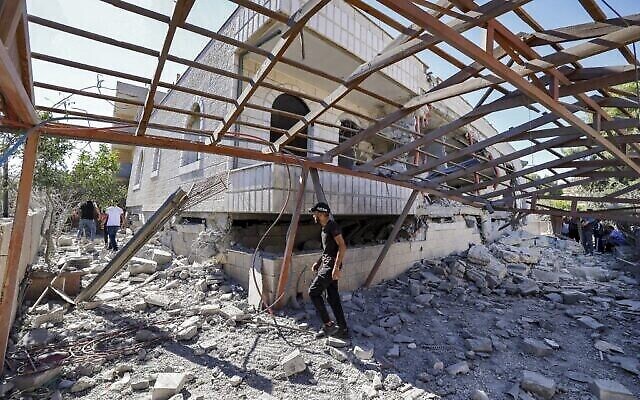 شاب فلسطيني يمر أمام مبنى يعود لمنتصر شلبي، المتهم بقتل طالب إسرائيلي في هجوم في مايو، بعد أن دمرته القوات الإسرائيلية في قرية ترمسعيا بالقرب من رام الله في الضفة الغربية، 8 يوليو، 2021.  (JAAFAR ASHTIYEH / AFP)