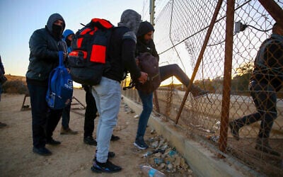عمال فلسطينيون من مدينة الخليل بالضفة الغربية يحملون متعلقاتهم الشخصية أثناء عبورهم إلى إسرائيل عبر ثقب في السياج الأمني بالقرب من مدينة الخليل بالضفة الغربية، 31 يناير، 2021. (Wisam Hashlamoun / Flash90)